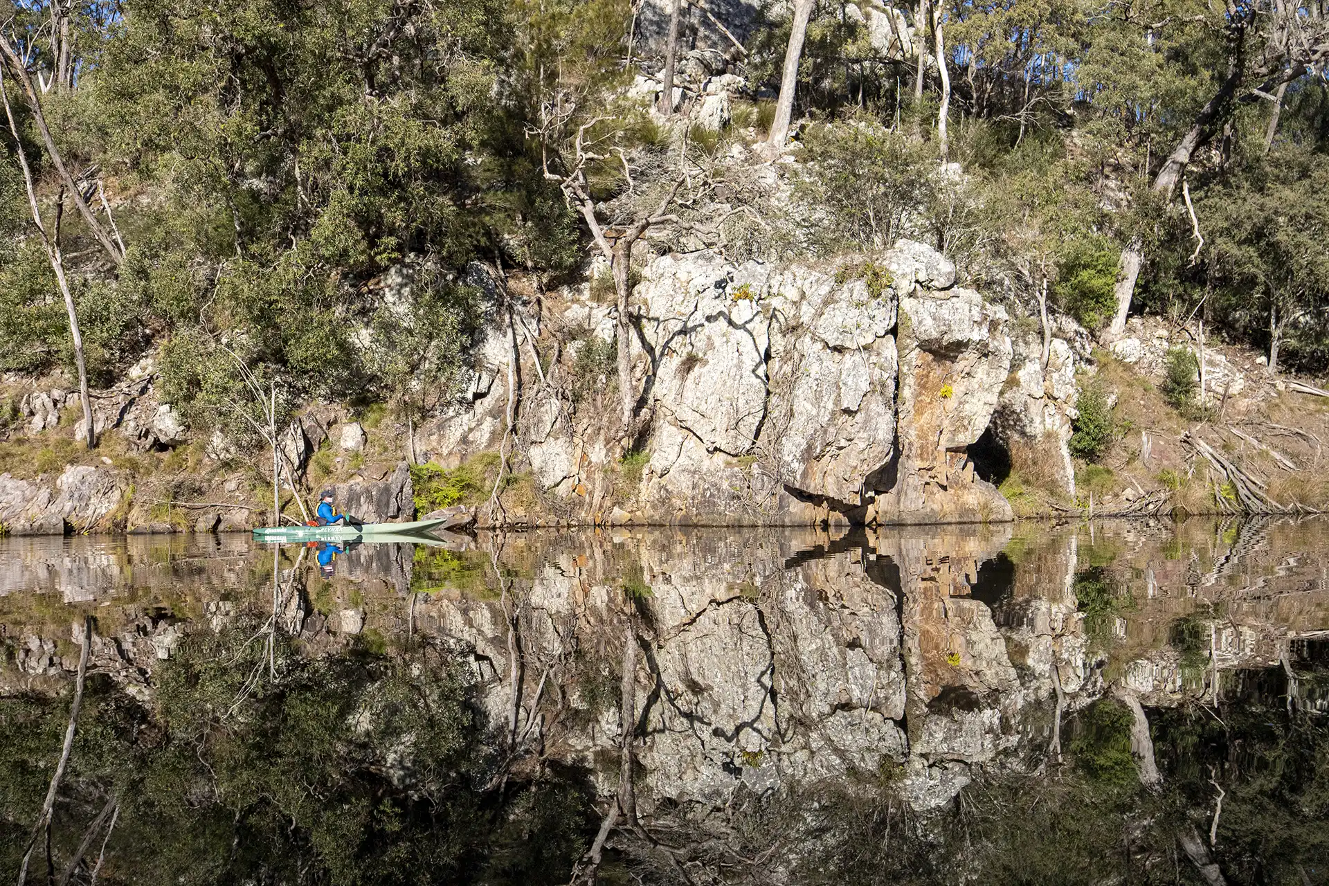 Kayak guide David reflected in Brogo Dam water, rock and tree reflections.