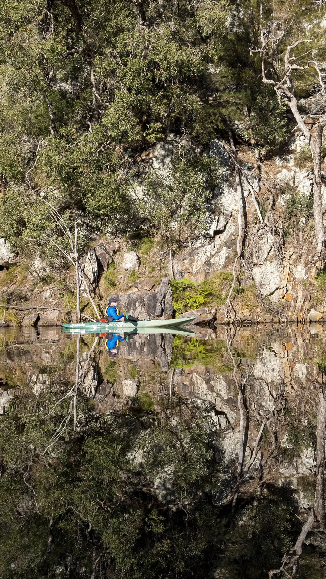 Kayak guide David reflected in Brogo Dam water, rock and tree reflections.